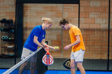 Riga, Letonya - 24 Ocak 2026: Padel turnuvası. Spor giyimli iki genç erkek sporcu, biri top, diğeri raket tutan bir Padel maçına hazırlanıyor.