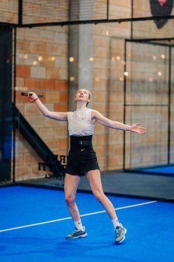 Riga, Letonya - 24 Ocak 2026: Padel turnuvası. Kolsuz tişörtlü ve şortlu bir bayan sporcu mavi bir kortta bir padel maçına hazırlanıyor.