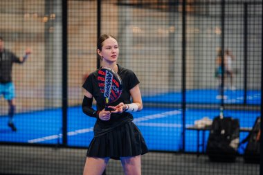 Riga, Letonya - 24 Ocak 2026: Padel turnuvası. Siyah kıyafetli kadın padel oyuncu, elinde bir raketle mavi kortta duruyor.