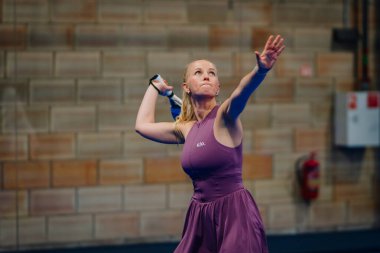 Riga, Letonya - 24 Ocak 2026: Padel turnuvası. Mor elbiseli bayan padel atlet, tuğla duvarlı kapalı bir spor tesisinde topa hizmet etmeye hazırlanıyor.