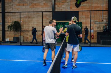 Riga, Letonya - 24 Ocak 2026: Padel turnuvası. Dört erkek Padel oyuncusu, arka planda izleyiciler olan mavi bir kortta birbirlerini selamlıyorlar.
