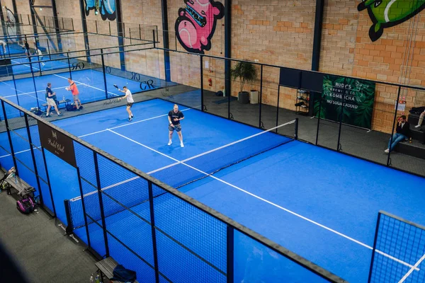 Riga, Letonya - 24 Ocak 2026: Padel turnuvası. Padel oyuncuları, renkli duvar sanatı ve eskrim sanatının yer aldığı bir spor tesisinde mavi sahada yarışıyorlar.