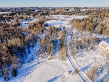 Karla kaplı tarlalar, dağınık ağaçlar ve dolambaçlı bir yol içeren kış manzarası kırsal bir ortamın sakinliğini vurguluyor.