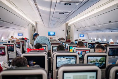 Dubai, Birleşik Arap Emirlikleri - 18 Ocak 2026: Yolcular, modern bir uçak ayarında kişisel ekranları ve tepe ışıkları olan bir uçak kabininde oturuyorlar