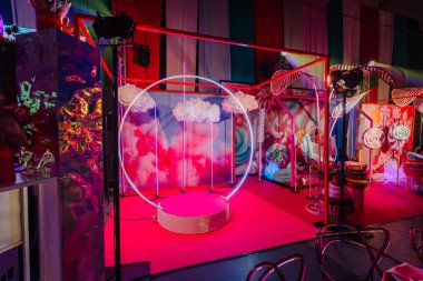 Dairesel neon ışığı, pembe halı ve şeker temalı dekorasyonlarla aydınlık bir etkinlik alanı, kutlamalar için canlı ve şenlikli bir ortam oluşturuyor.