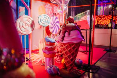 Büyük boy dondurma külahı ve büyük lolipoplar, neşeli bir atmosferdeki parlak ışıklarla aydınlatılmış pembe zeminde canlı bir tatlı temalı ekran oluşturur.