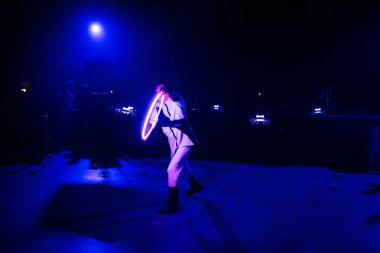 Riga, Letonya - 30 Ocak 2026: Şeker Diyarı. Beyaz kostümlü bir sanatçı, sahnede parlak bir hula çemberi çeviriyor. Karanlık bir mekanda mavi ışık yanıyor.