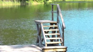 Tahta adımlar durgun göl suyuna iniyor, canlı yeşilliklerle çerçevelenmiş, doğal bir çevrede huzurlu bir anı yakalıyor.