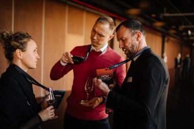 Riga, Letonya - 4 Şubat 2026: Chery. Üç profesyonel Chery TIGGO modelleri hakkında şarap kadehleri tutan bir tanıtım etkinliği sırasında sohbet ediyorlar.