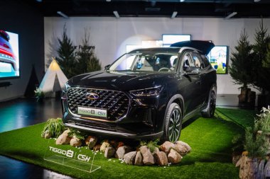 Riga, Letonya - 4 Şubat 2026: Chery. Chery TIGGO 8 CS SUV modern bir sergi alanında dekoratif taşlar ve dijital ekranlarla çimlerde sergilendi