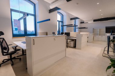 Beyaz kabinleri ve ergonomik sandalyeleri olan çağdaş ofis alanı, büyük pencerelerden gelen doğal ışıkla aydınlatılmış, temiz ve düzenli bir ortam sergiliyor