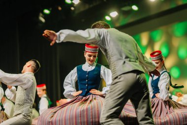 Valmiera, Letonya - 27 Aralık 2025 Letonya Halk Dansı Konseri. Geleneksel giyinmiş Letonyalı halk dansçıları, performanslarını aydınlatan parlak ışıklarla yeteneklerini sahnede sergiliyorlar.