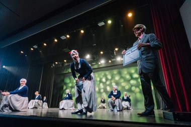 Valmiera, Letonya - 27 Aralık 2025 Letonya Halk Dansı Konseri. Letonyalı halk sanatçıları geleneksel giysiler içinde renkli ışıklandırma ve oturma izleyicileri ile sahnede.