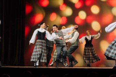 Valmiera, Letonya - 27 Aralık 2025 Letonya Halk Dansı Konseri. Geleneksel kostümlü Letonyalı dansçılar sahnede canlı ışıklandırma ve şenlikli bir atmosferle performans sergiliyorlar.
