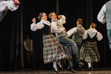 Valmiera, Letonya - 27 Aralık 2025 Letonya Halk Dansı Konseri. Geleneksel kostümlü Letonyalı halk dansçıları sahnede enerjik bir şekilde sahne alıyorlar.