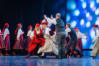 Valmiera, Letonya - 27 Aralık 2025 Letonya Halk Dansı Konseri. Geleneksel giyinmiş Letonyalı halk dansçıları yeteneklerini sahnede parlak ışıklandırma ve renkli kostümlerle sergiliyorlar.