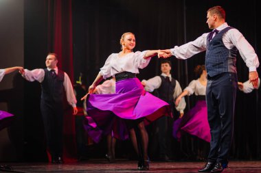 Valmiera, Letonya - 27 Aralık 2025 Letonya Halk Dansı Konseri. Canlı kostümler içindeki Letonyalı halk dansçıları dramatik ışıklandırmayla geleneksel dansı sahnede sergilediler.