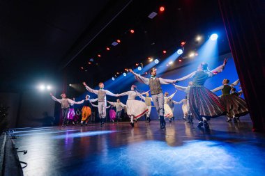 Valmiera, Letonya - 27 Aralık 2025 Letonya Halk Dansı Konseri. Geleneksel giyinmiş Letonyalı halk dansçıları, performanslarını aydınlatan parlak ışıklarla yeteneklerini sahnede sergiliyorlar.