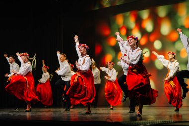 Valmiera, Letonya - 27 Aralık 2025 Letonya Halk Dansı Konseri. Geleneksel giyinmiş Letonyalı halk dansçıları renkli ışıklandırmalarla performanslarını sahnede sergiliyorlar.