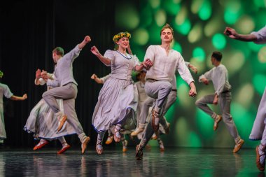 Valmiera, Letonya - 27 Aralık 2025 Letonya Halk Dansı Konseri. Geleneksel giyinmiş Letonyalı halk dansçıları canlı bir ışık ve canlı bir atmosferle sahnede gösteri yapıyorlar.