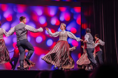 Valmiera, Letonya - 27 Aralık 2025 Letonya Halk Dansı Konseri. Geleneksel giyinmiş Letonyalı halk dansçıları renkli ışıklandırma ve festival atmosferiyle sahnede gösteri yapıyorlar.