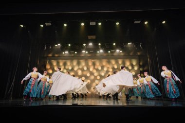 Valmiera, Letonya - 27 Aralık 2025 Letonya Halk Dansı Konseri. Canlı kostümler içindeki geleneksel halk dansçıları, gösteriyi aydınlatan parlak ışıklarla zarif bir şekilde sahneye çıkıyorlar.