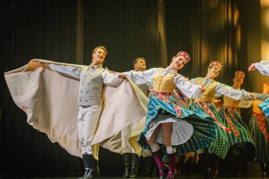 Valmiera, Letonya - 27 Aralık 2025 Letonya Halk Dansı Konseri. Geleneksel halk dansçıları sahnede dramatik ışıklandırmalarla gösteri yaparken renkli kostümler ve akıcı giysiler sergilerler.