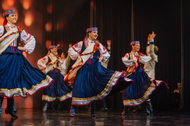 Valmiera, Letonya - 27 Aralık 2025 Letonya Halk Dansı Konseri. Geleneksel kostümlü halk dansçıları yeteneklerini renkli ışıklandırma ve izleyiciler eşliğinde sahnede sergiliyorlar.