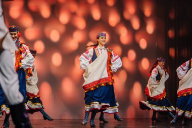 Valmiera, Letonya - 27 Aralık 2025 Letonya Halk Dansı Konseri. Geleneksel renkli kostümlü halk dansçıları arkalarında parlak ışıklarla sahnede enerjik bir performans sergiliyorlar.