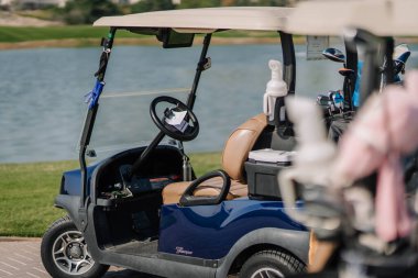 Dubai, Birleşik Arap Emirlikleri - 13 Ocak 2026: Golfmatchplay. Kahverengi koltuklu golf arabası arka planda golf sopaları olan bir gölün yanında park halinde.