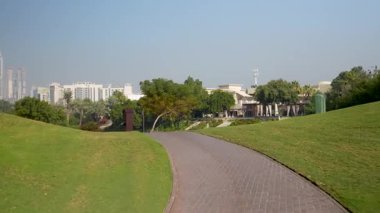Dubai, Birleşik Arap Emirlikleri - 13 Ocak 2026: Dubai 'nin ufuk çizgisi ve arka planında bir su özelliği olan bir parktaki dolambaçlı bir yolun manzarası