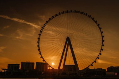 Dubai, Birleşik Arap Emirlikleri - 14 Ocak 2026: Gün batımında büyük bir dönme dolabın silüeti, arka planda kentsel binalar, canlı bir ufuk çizgisi sergiliyor