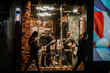 Dubai, Birleşik Arap Emirlikleri - 14 Ocak 2026: Berber dükkanı sahnesinde iki berber dışarıda yayalar ve iyi ışıklandırılmış bir mağazanın içinde saç kesiyor