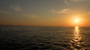 Dubai, Birleşik Arap Emirlikleri - 14 Ocak 2026: Suda süzülen bir tekneyle günbatımı, dalgalarda parıldayan altın yansımalar