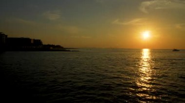 Dubai, Birleşik Arap Emirlikleri - 14 Ocak 2026: Okyanus yüzeyini aydınlatan gün batımı, kıyı boyunca siluetli binalar boyunca su üzerinde hareket eden bir tekne gibi