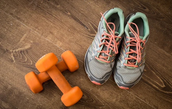 Spor ayakkabı, ahşap arka plan üzerinde turuncu dumbbells çifti.