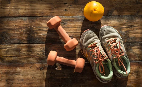 Zapatillas de deporte, par de pesas de color naranja y pomelo sobre fondo de madera. Pesas para un entrenamiento de fitness . Imagen de archivo