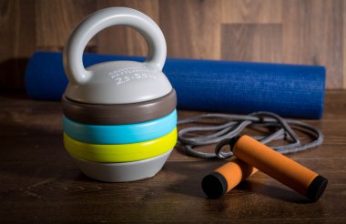 Ahşap arka plan üzerinde atlama ipi ve mat fitnes için ayarlanabilir kettlebell. Bir fitness eğitimi için ağırlıklar.
