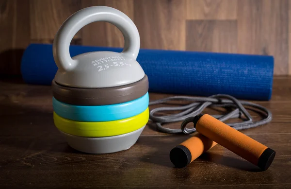 Ahşap arka plan üzerinde atlama ipi ve mat fitnes için ayarlanabilir kettlebell. Bir fitness eğitimi için ağırlıklar.