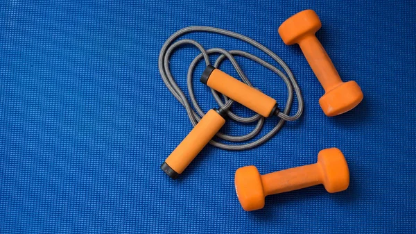 Çift turuncu dumbell ve mavi yoga mat zemin üzerine ip atlama
