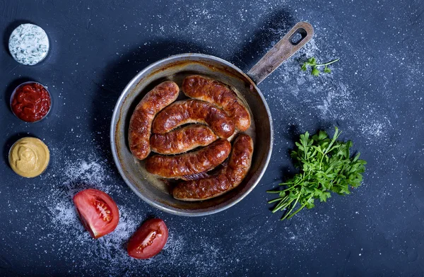 Pişmiş sosis kızartma tavası, üç et sosu, domates ve yeşillik karanlık bir arka plan üzerinde. Lezzetli ve sağlıklı et yemek.