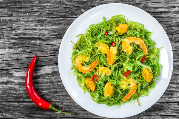 Deliciosa salada de camarões, mexilhões, algas marinhas, pimenta e gergelim temperado com azeite extra virgem no prato branco na velha mesa de madeira, vista superior — Fotografia de Stock