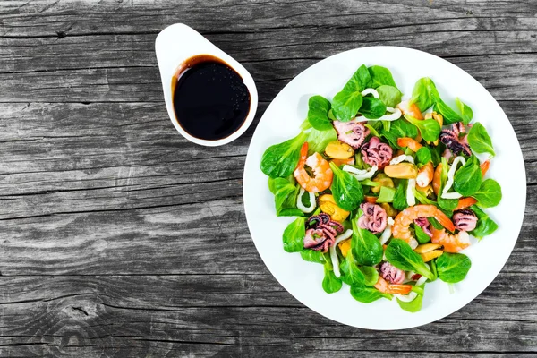 Салат з морепродуктів зі свіжим зеленим листям на білій страві з оливковою олією, вид зверху — стокове фото