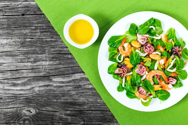 Seafood salad with fresh green leaves on the white dish with olive oil, top view — Stockfoto