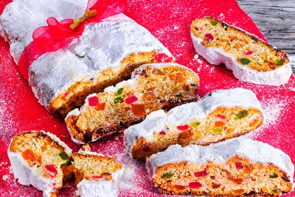 Рождественский Столлен, традиционный немецкий рождественский торт с сухофруктами, орехами, специями и сахарной глазурью, украшенный красными и золотыми лентами, горизонтальным крупным планом — стоковое фото