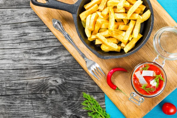 Kartoffelfrites mit Chilistücken auf der weißen Schüssel und marinierte norwegische Heringsscheiben in Tomatensauce auf den Roggenbrotstücken, Glasgefäß mit leckerem Hering mit Dill, von oben — Stockfoto