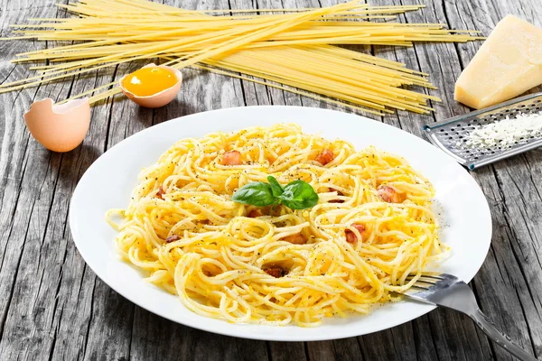 Spaghetti carbonara, basil, eggs yolk, grated parmesan cheese, bacon, close-up — Stock Photo, Image