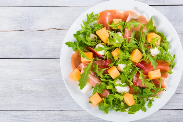 Rucola, mozzarella en prosciutto en meloen salade, bovenaanzicht — Stockfoto