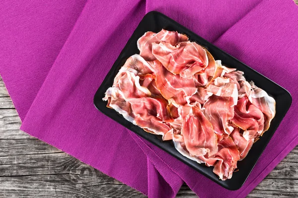 Üzerinde siyah dikdörtgen yemek lezzetli Prosciutto dilim kıvrılmış — Stok fotoğraf