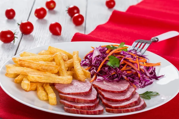 Filé de vitela defumado fatiado, batatas fritas e salada de repolho vermelho com cenouras cortadas em tiras e molho de salsa com vinagre e azeite em tapete de mesa com tomate cereja em tábuas brancas rústicas, close-up — Fotografia de Stock